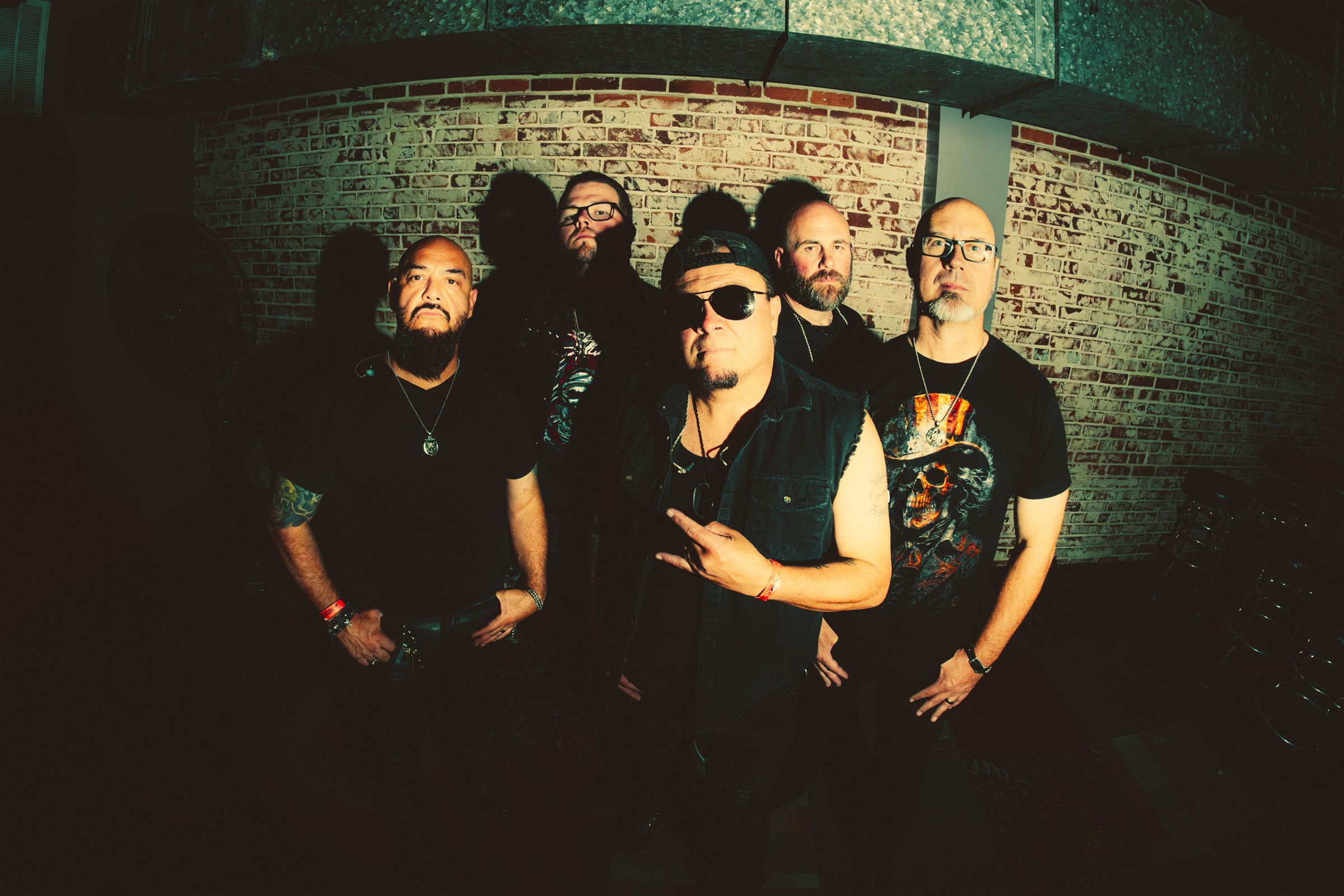 TangenT, all five members against a brick wall, the singer throwing horns