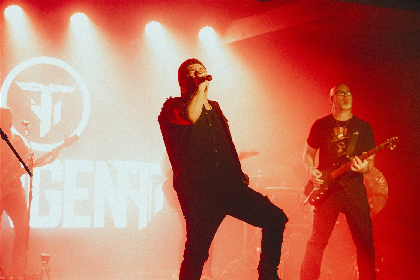 Singer and guitarist under red light in front of the TangenT logo