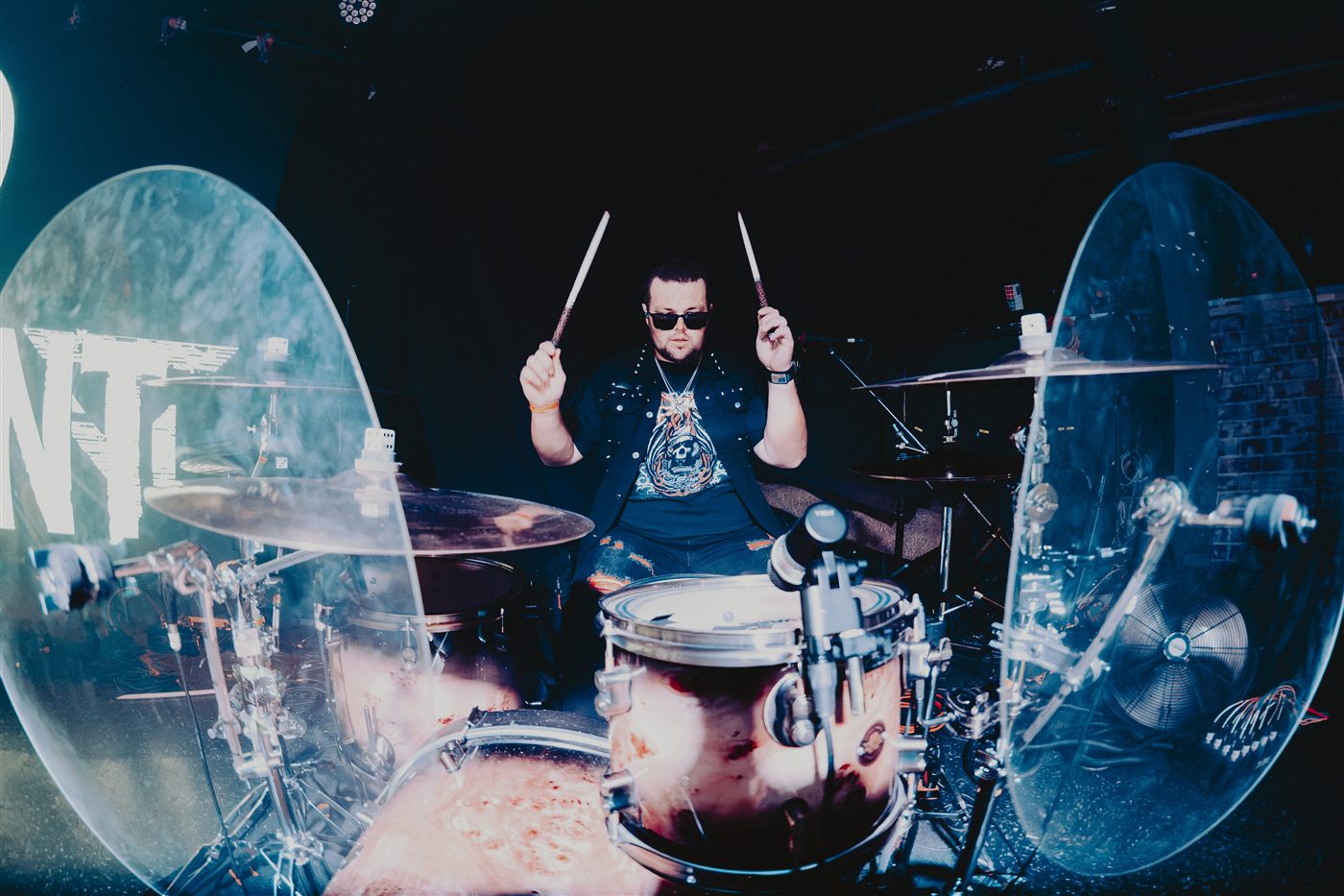 Drummer mid-hit behind a clear drum shield